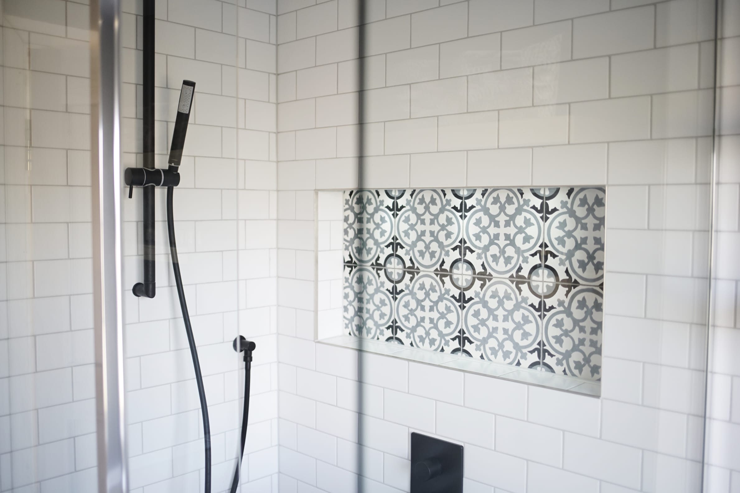 Modern shower featuring white tiles and an ornate patterned inset. Black fixtures present.