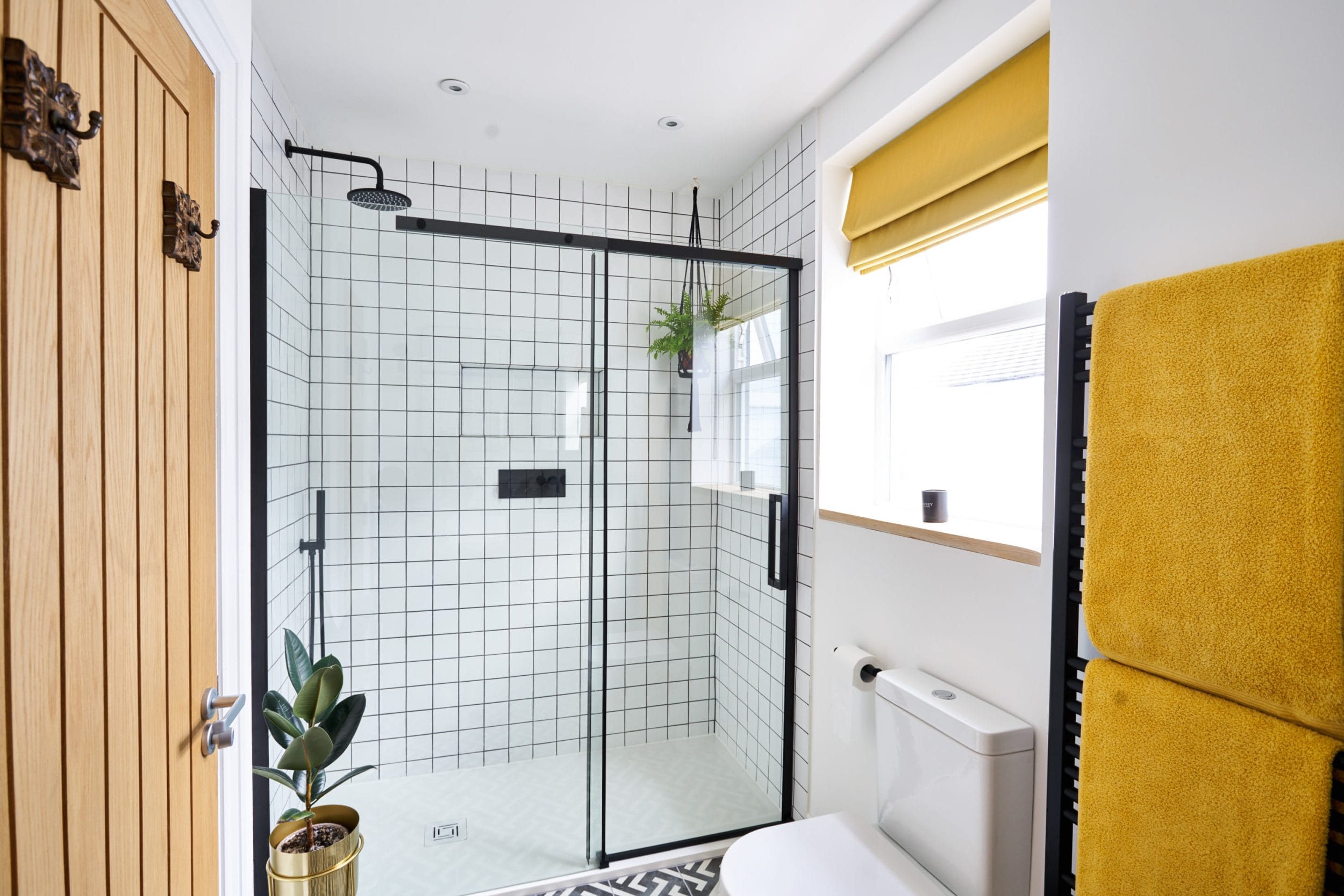 Modern bathroom featuring a glass shower, yellow towels, and tiled walls.