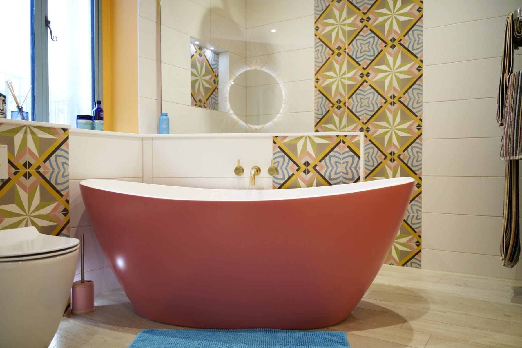 A modern bathroom featuring a pink freestanding bathtub and decorative patterned tiles.