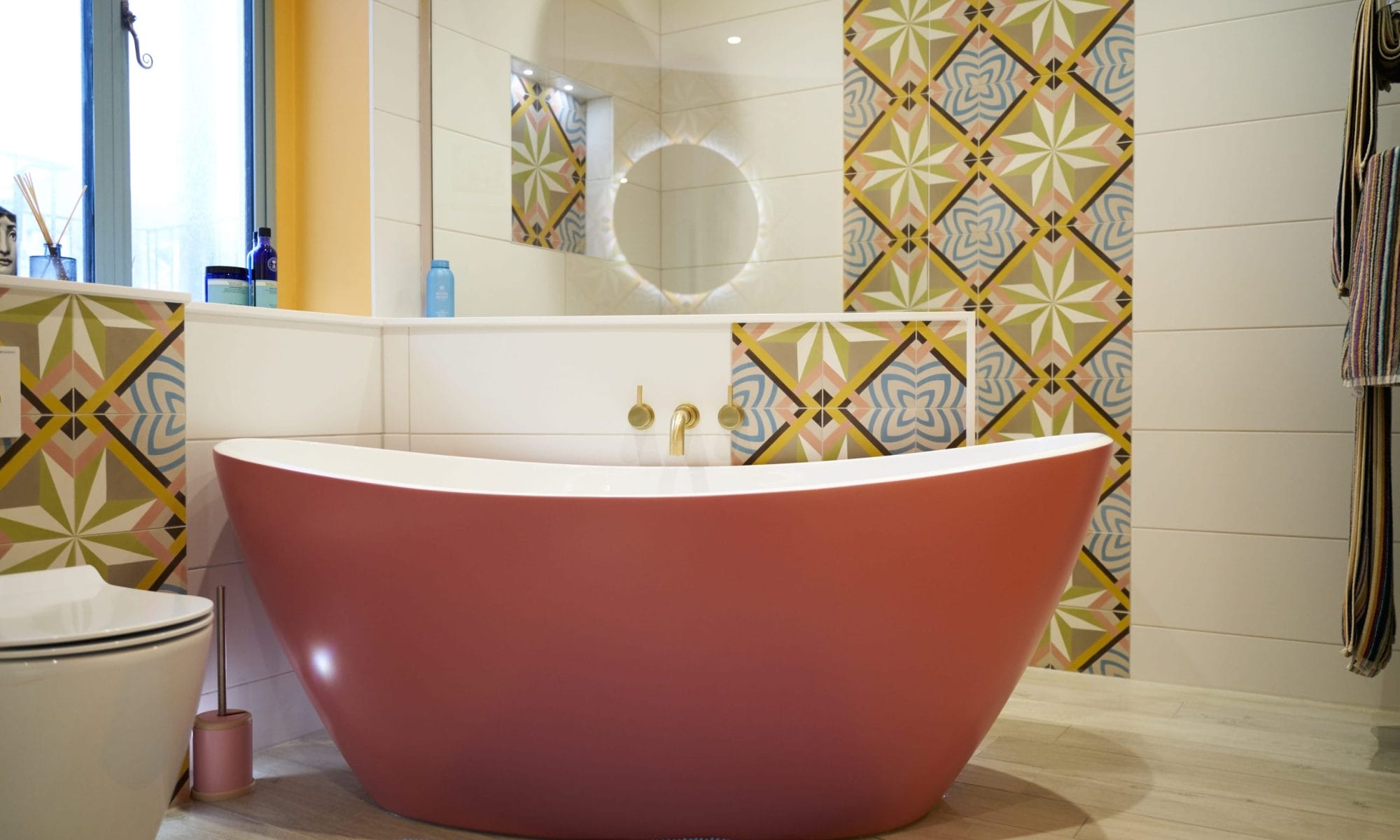 A modern bathroom featuring a pink freestanding bathtub and decorative patterned tiles.
