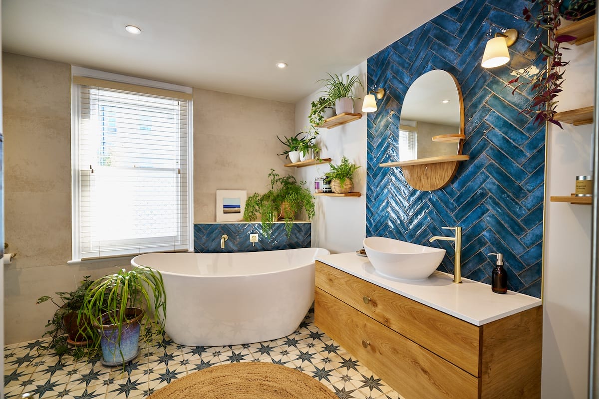 Bright modern bathroom with a large free-standing bath, wooden vanity, and bold blue herringbone tile wall