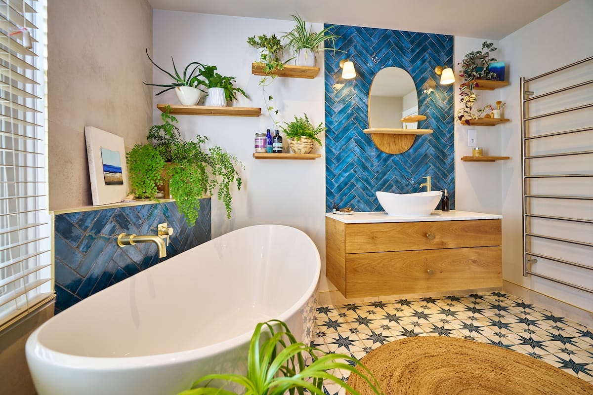 Modern bathroom featuring a free-standing bathtub, blue herringbone tiles, and wooden vanity with shelving and plants