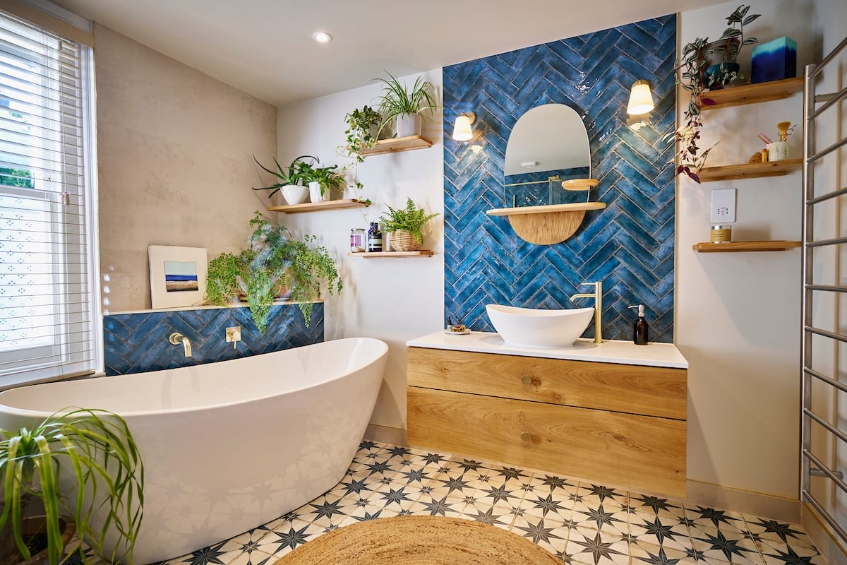 Modern bathroom featuring a free-standing bathtub, blue herringbone tiles, and wooden vanity with shelving and plants