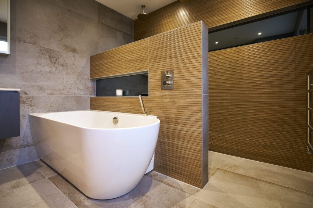 Large freestanding bath in a contemporary bathroom with wood-effect wall tiles and brushed nickel fixtures