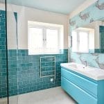 A modern bathroom featuring teal wall tiles, a matching vanity unit, a walk-in shower, and decorative fish-themed wallpaper