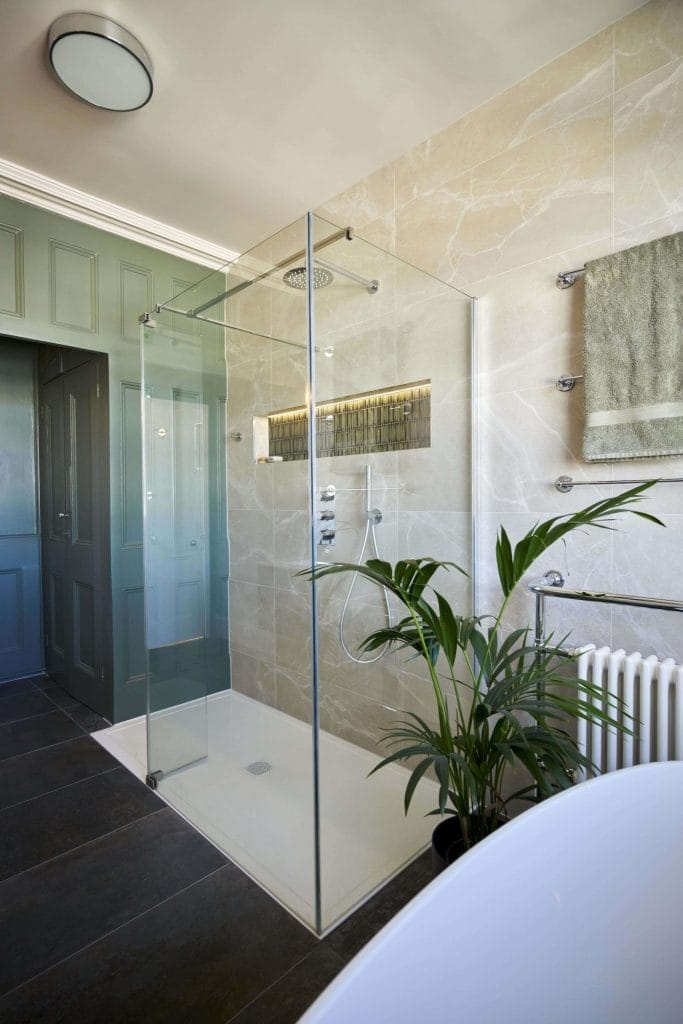 Stylish bathroom with a glass-enclosed shower, floating vanity, and freestanding bathtub, showcasing green accents and natural stone tiles.