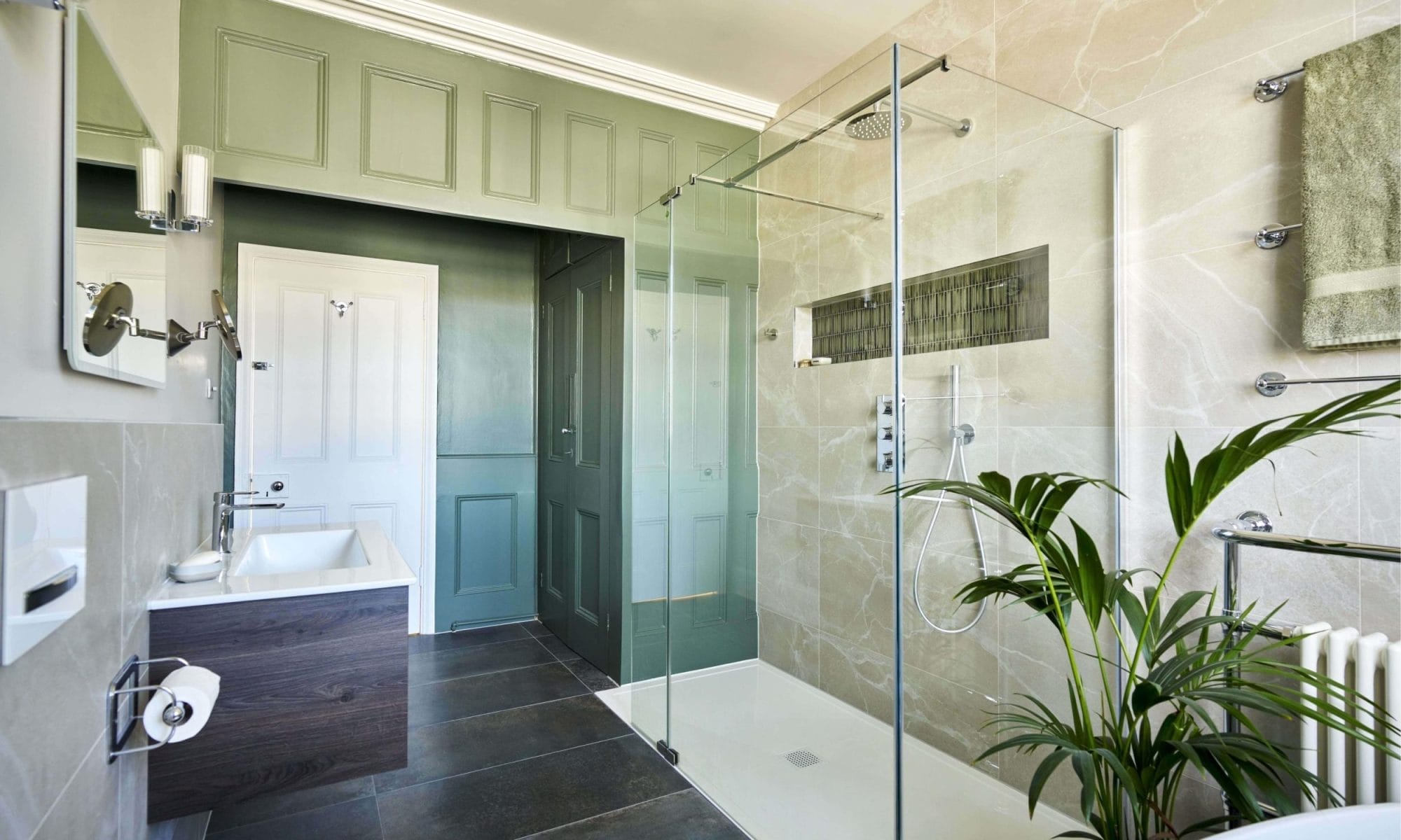 Contemporary bathroom with a glass shower enclosure, green paneling, and natural stone wall tiles.