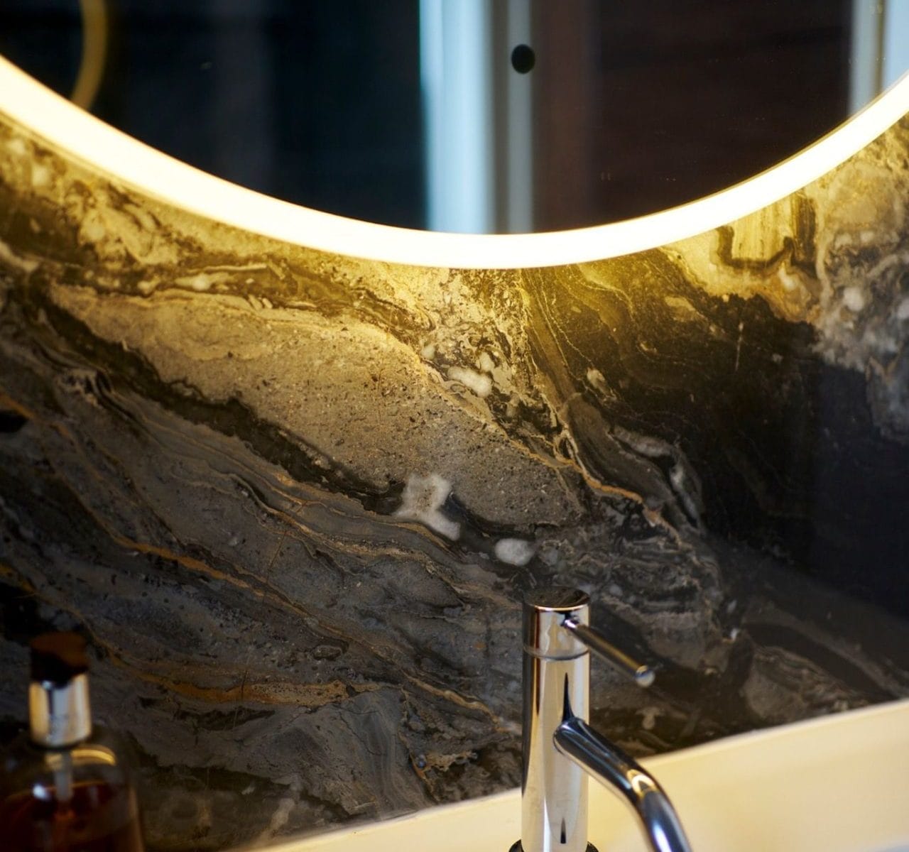 Close-up of chrome mixer tap and white ceramic basin with marble backsplash