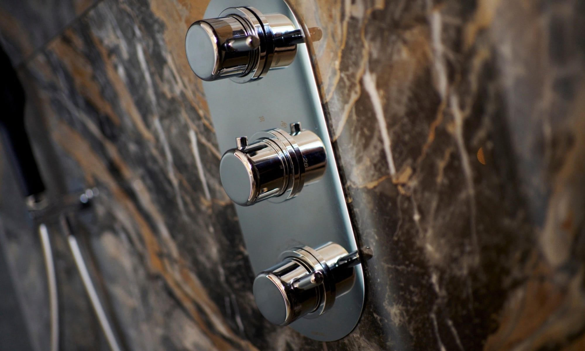 Minimalist chrome shower valve controls on marble wall tiles