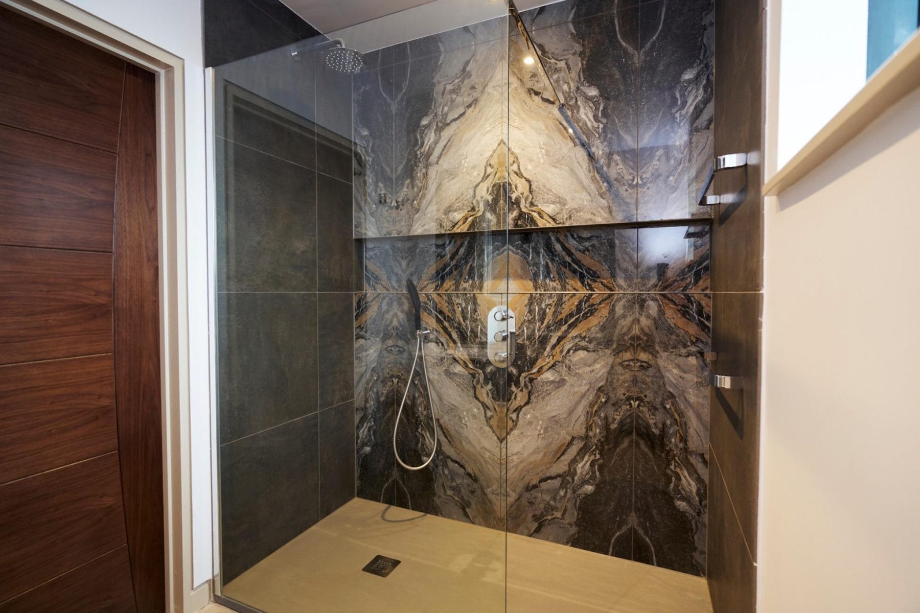 Spacious walk-in shower with striking bookmatched marble-effect tiles in a luxury Sussex en-suite