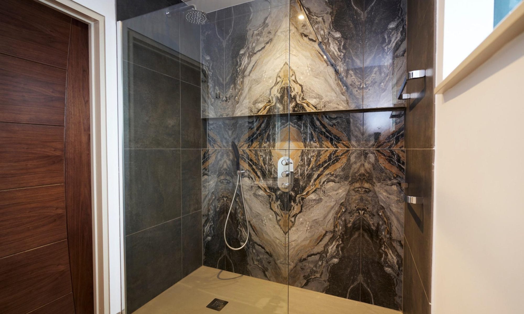 Spacious walk-in shower with striking bookmatched marble-effect tiles in a luxury Sussex en-suite