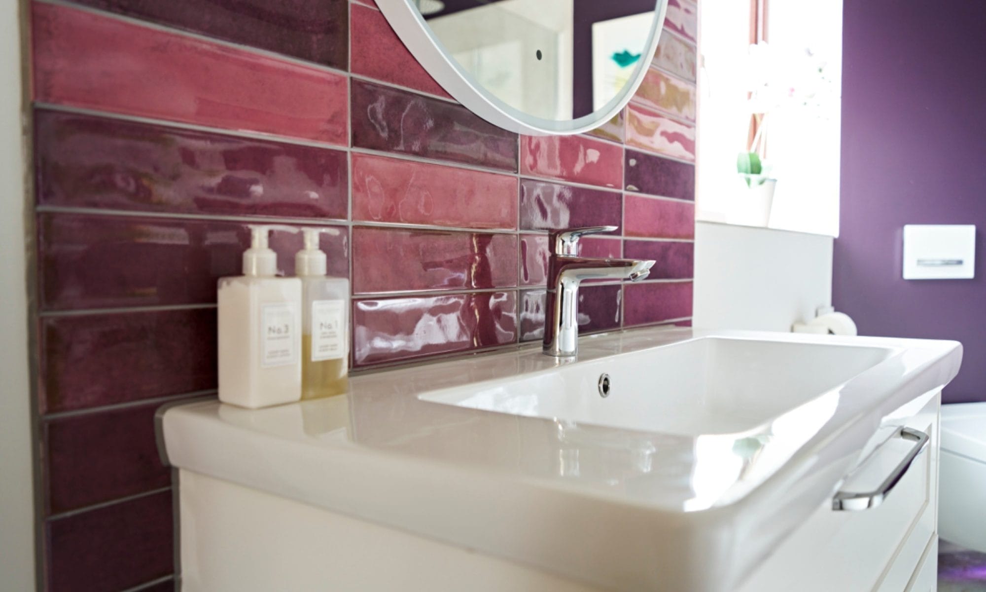 Purple glazed wall tiles with round mirror and white basin