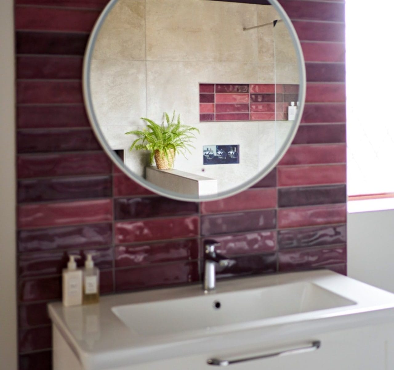 Round mirror reflecting purple tiles and fern in luxury en-suite