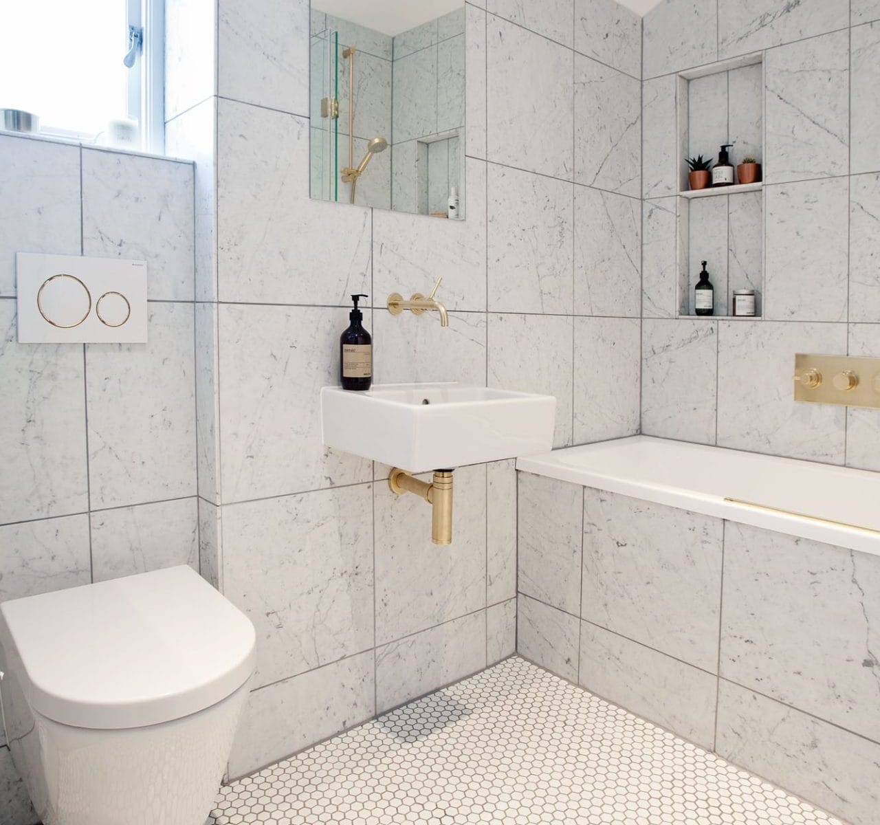 A Modern family bathroom with marble tiles, gold fixtures for a luxury feel, and hexagon floor tiles. Marble sled niches provides minimalistic storage