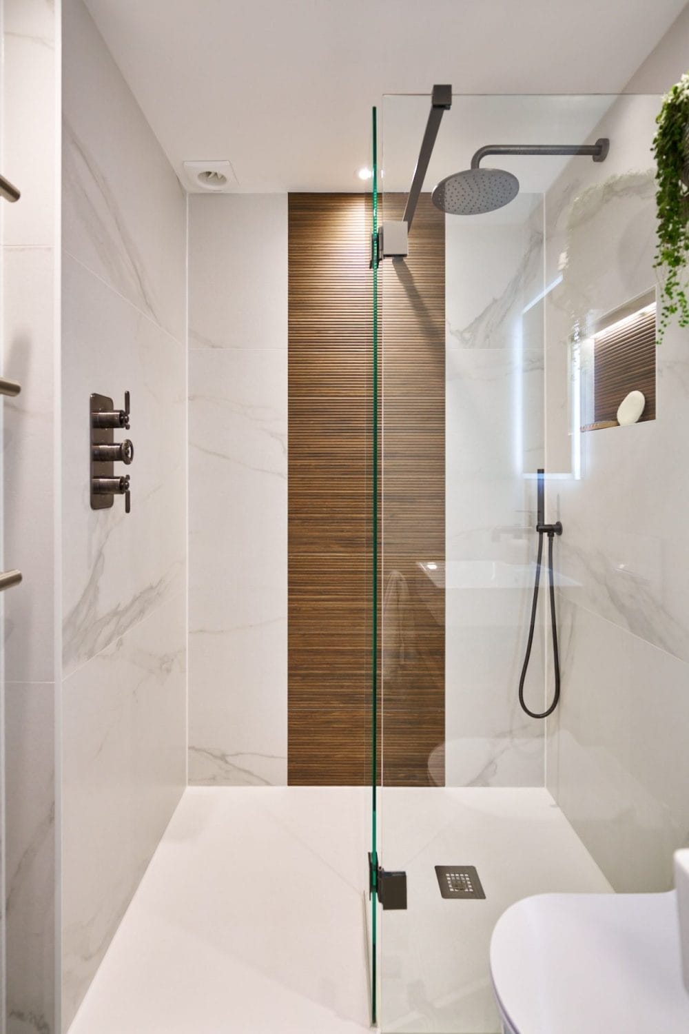 Frameless wet room shower with ribbed wood accent strip, marble‑effect walls and ceiling‑mounted rainfall head.