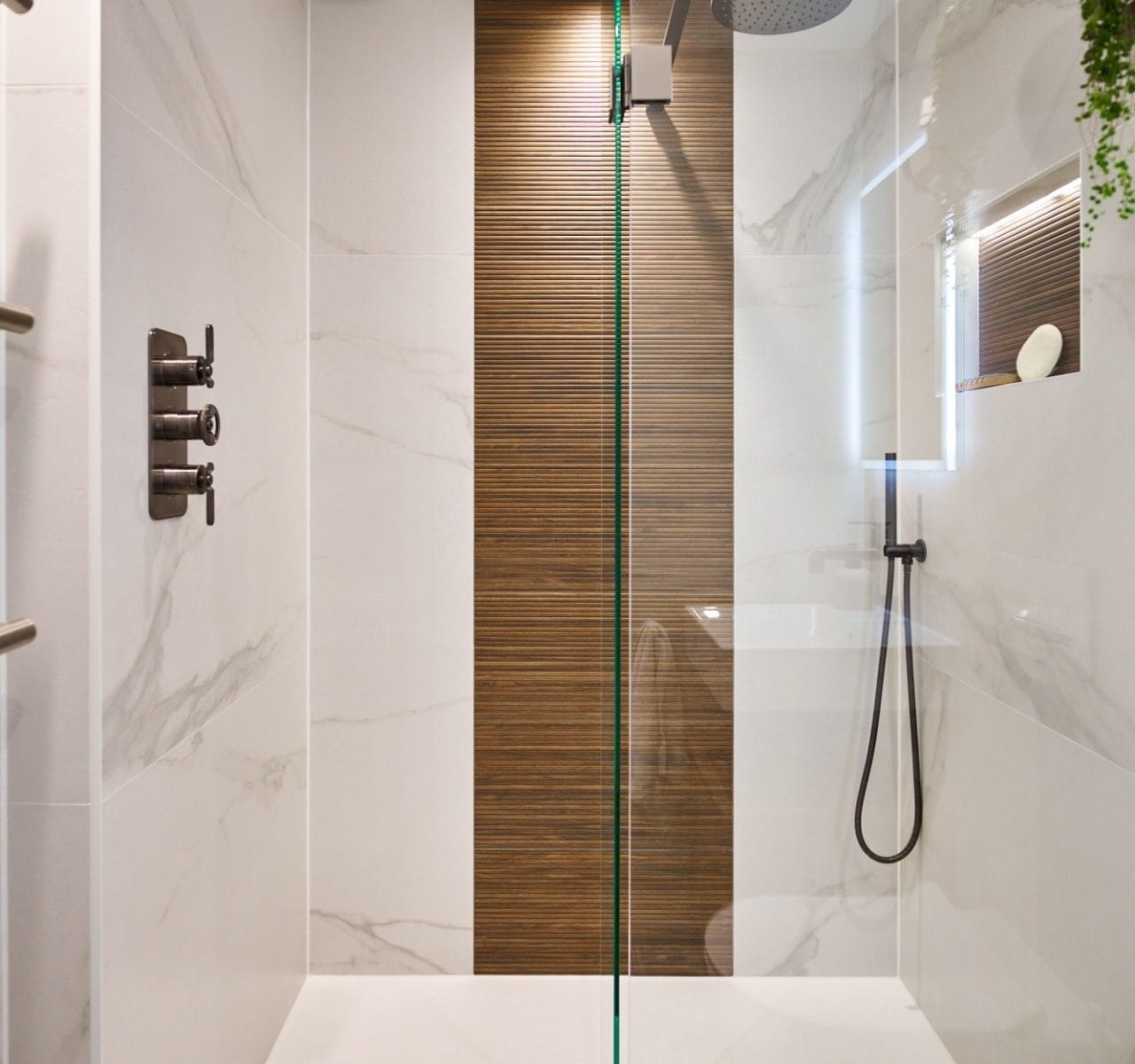 Frameless wet room shower with ribbed wood accent strip, marble‑effect walls and ceiling‑mounted rainfall head.