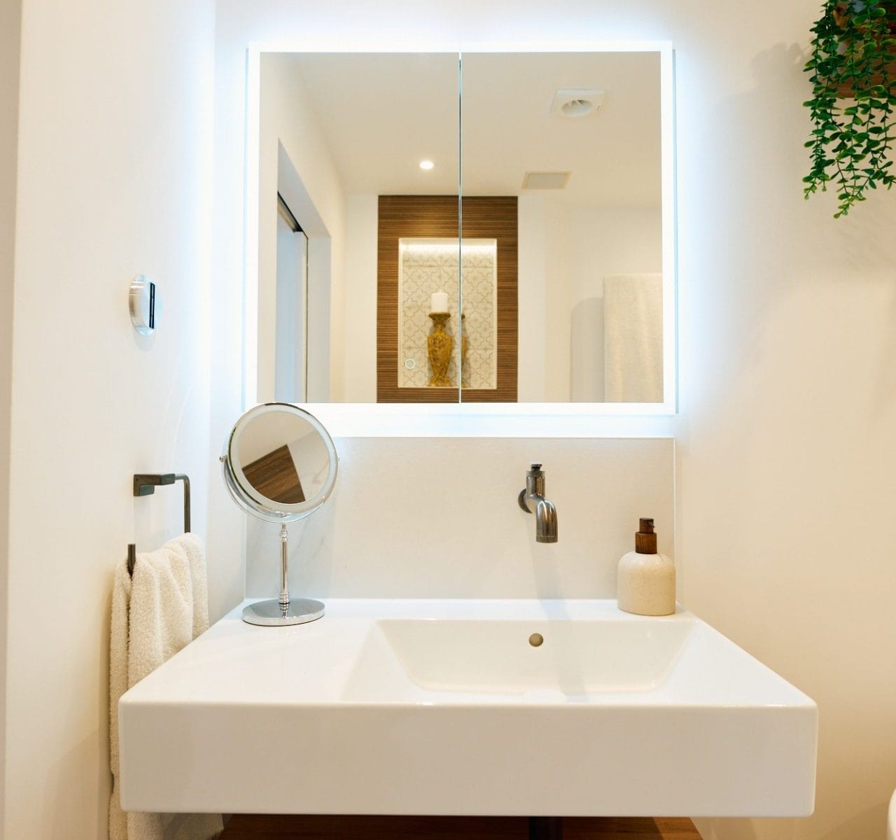 Floating vanity with illuminated mirror reflecting wood‑slat accent and tiled display niche in a contemporary Sussex bathroom.