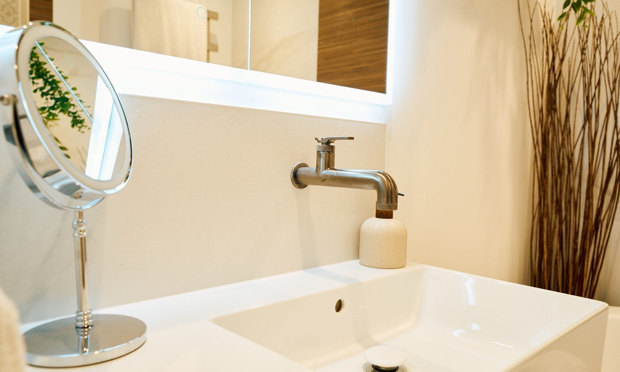 Detail of wall‑mounted basin tap with illuminated mirror above in a light, modern Sussex bathroom.