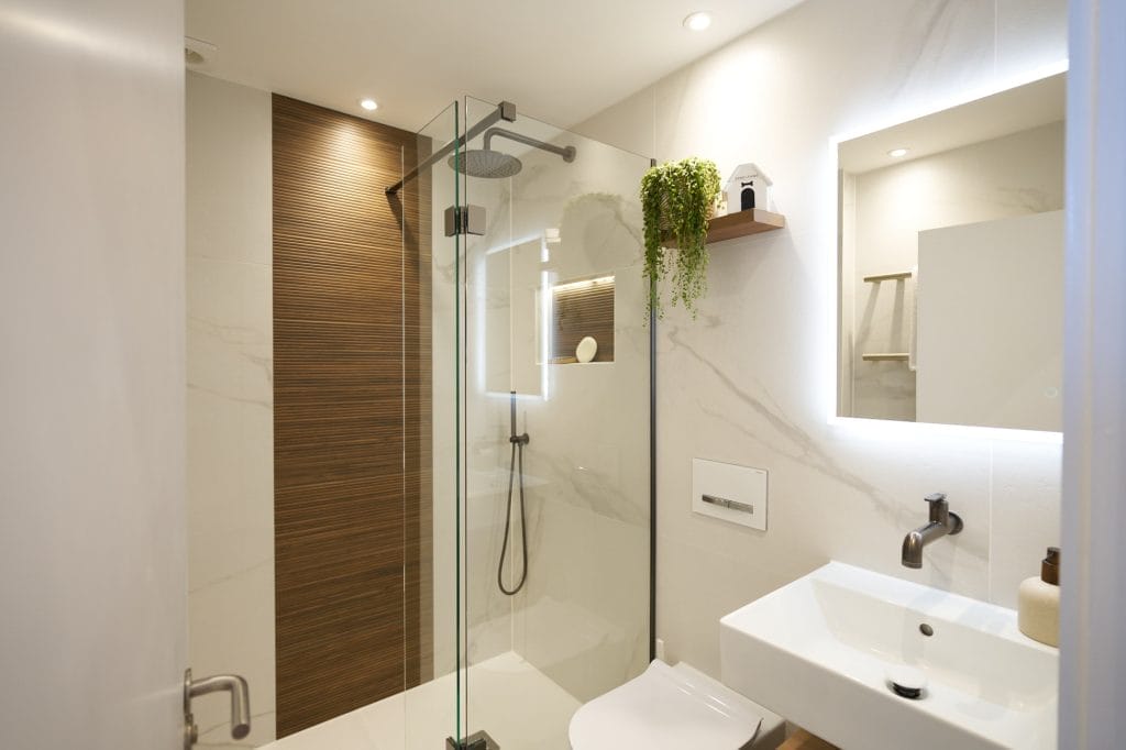 Walk‑in shower with large marble‑effect tiles, ribbed wood accent panel and black rainfall shower head.
