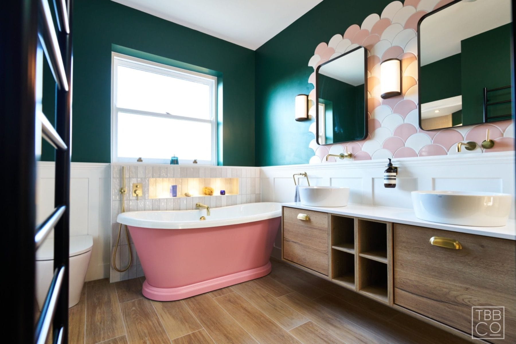 Bathroom featuring double vanity, pink scalloped tiles, green wall, and dual mirrors with brass taps.